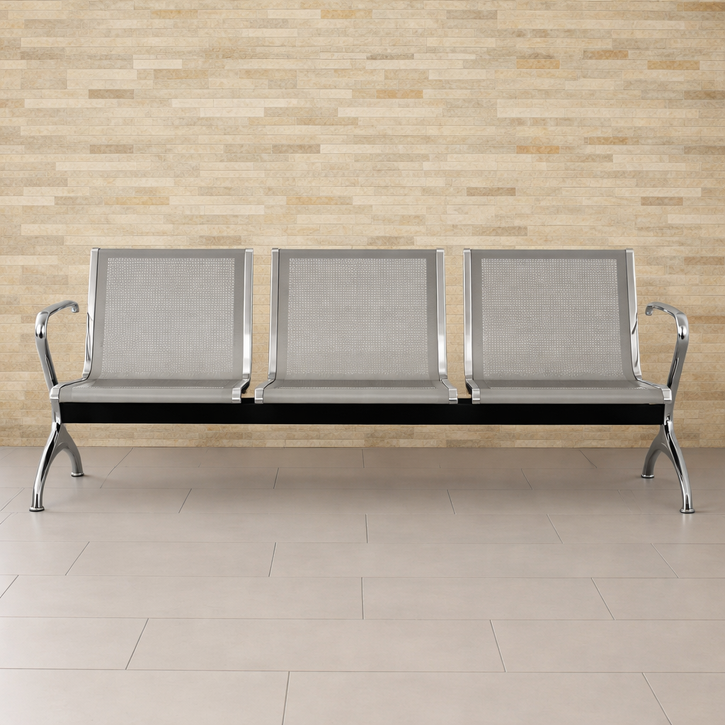 En la imagen se observa un área de espera de hospital, donde hay bancas metálicas grises dispuestas para los pacientes. Al fondo, se puede ver personal médico que se mueve por el entorno, creando un ambiente de atención y cuidado.